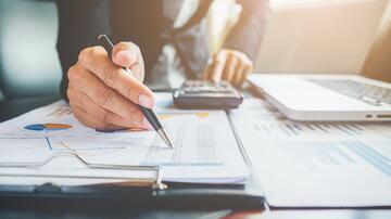 Hand schrijft op een document naast een laptop en rekenmachine.