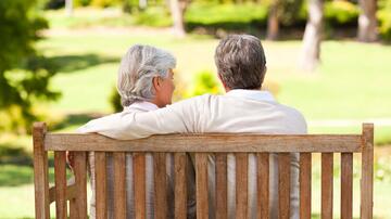 Ouder stel zittend op bank in zonnig park, omarmend.