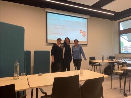 Drie mensen staan voor een scherm in een vergaderruimte.