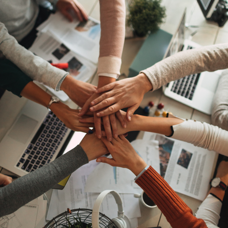 Handen gestapeld boven laptops op een kantoorbureau, samenwerking.