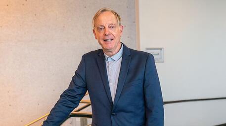 Man in pak lacht, staand in moderne ruimte.