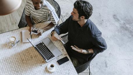 Twee mensen werken samen aan een laptop aan tafel.