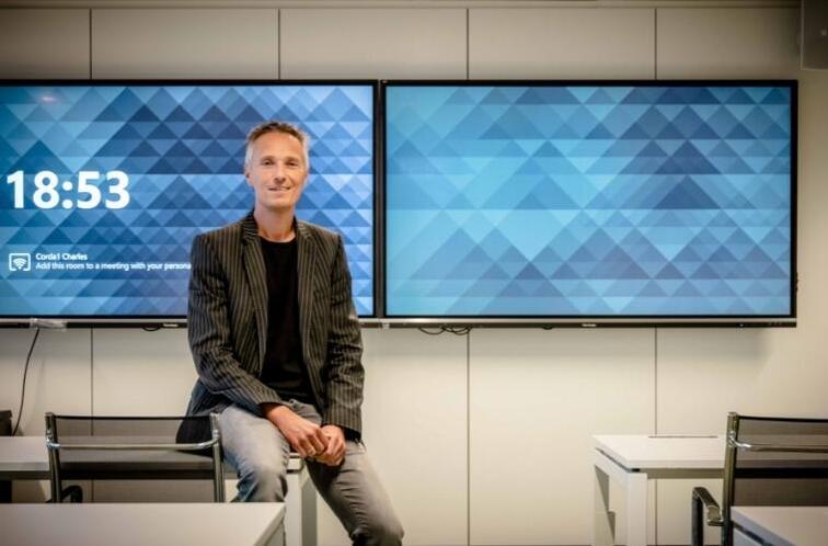 Man zit op bureau in kantoor met twee schermen op de achtergrond.