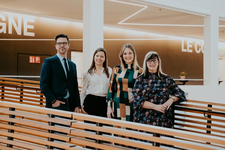 Vier mensen in zakelijke kleding staan bij een houten railing in een moderne ruimte, glimlachend.