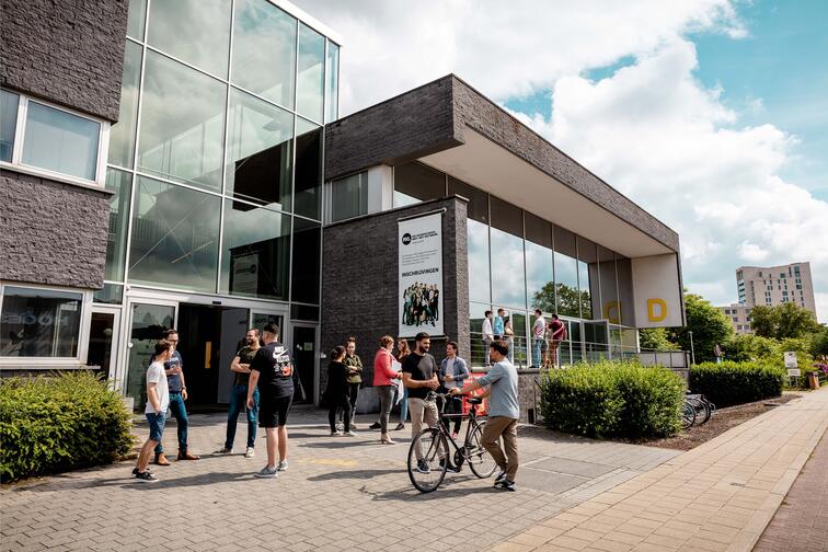 Mensen verzamelen zich voor een modern gebouw op een zonnige dag.