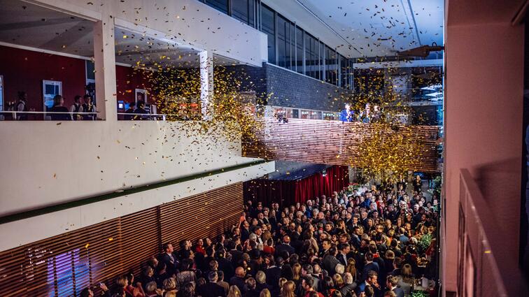 Grote menigte mensen in hal met vallende confetti. Feestelijke sfeer.