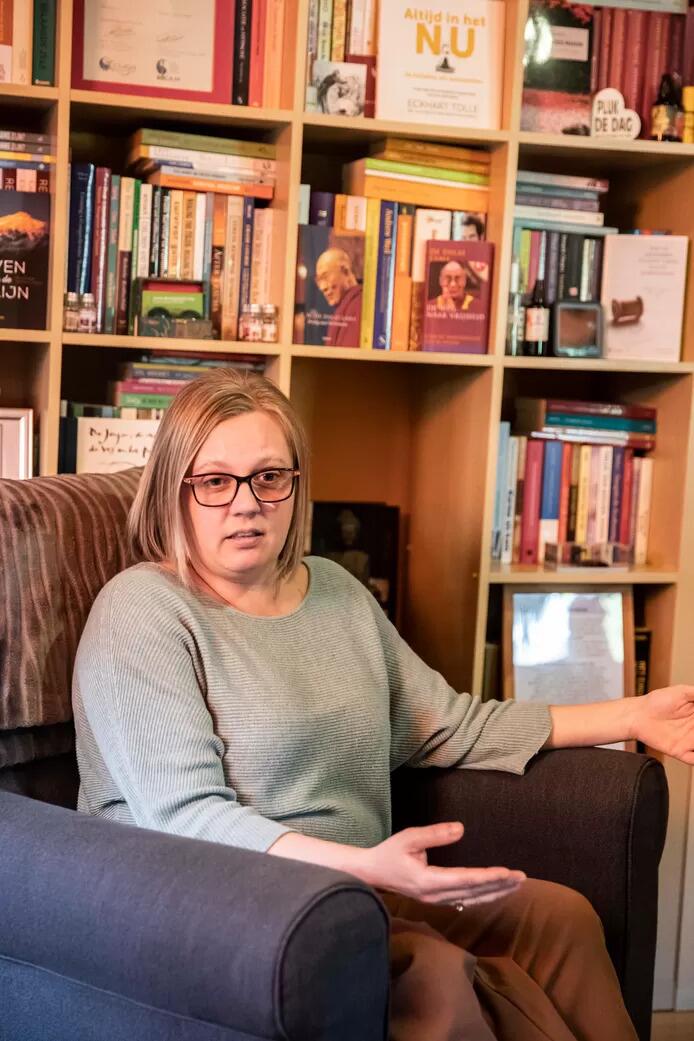 Vrouw in fauteuil voor boekenplank, kijkt ontspannen.