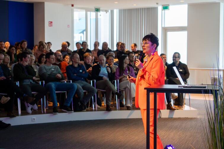 Spreker in feloranje pak presenteert voor een aandachtig publiek in een zaal.