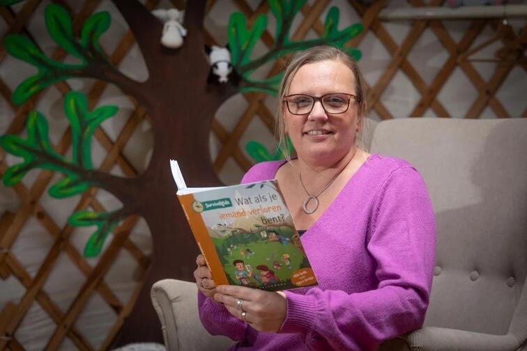 Persoon leest een boek in een stoel voor een muur met boomdecoratie.