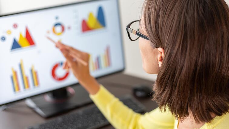 Vrouw met bril wijst naar kleurrijke grafieken op computerscherm.