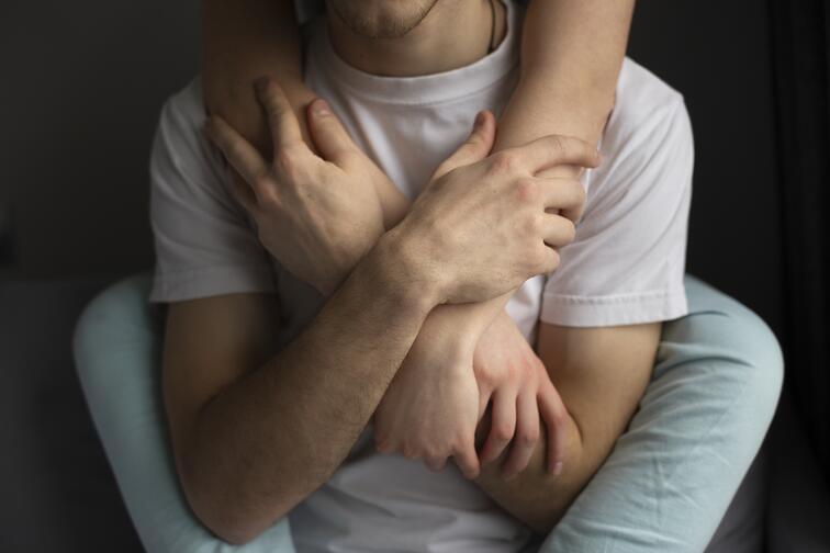 Persoon omhelst iemand, handen gekruist op borst, donkere achtergrond.