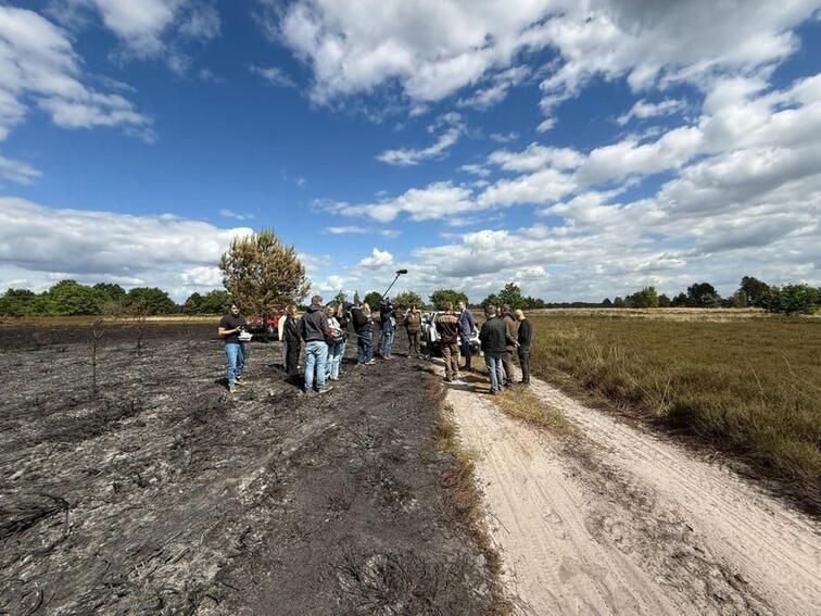 Groep mensen loopt op zandweg in natuurgebied onder zonnige wolkenhemel.